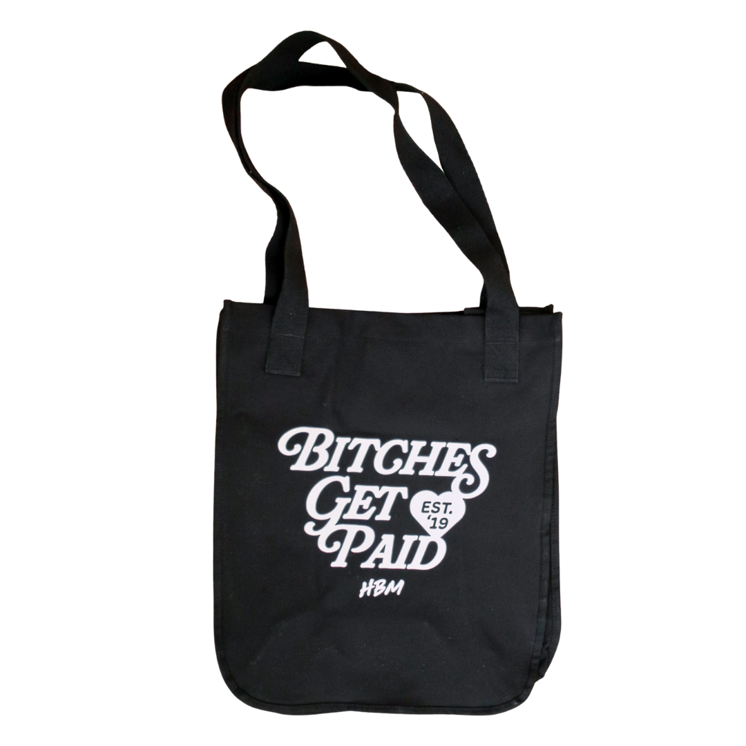 A black canvas tote bag with white printed text reading 'BITCHES GET PAID' and a small 'HBM' logo, shown on a plain white background.